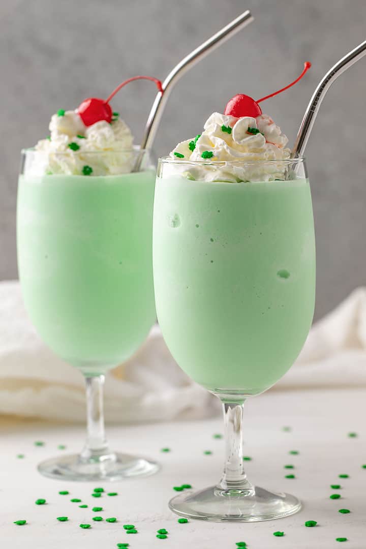 2 shamrock milkshakes topped with whipped topping and cherries in glasses with stainless steel straws.  