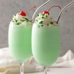 2 shamrock shakes topped with whipped topping, green sprinkles and a maraschino cherry. Overlay text at top of image.