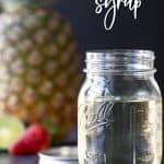 A Mason jar filled with simple syrup. A pineapple, lime and strawberry are in the background. Overlay text at top of image.