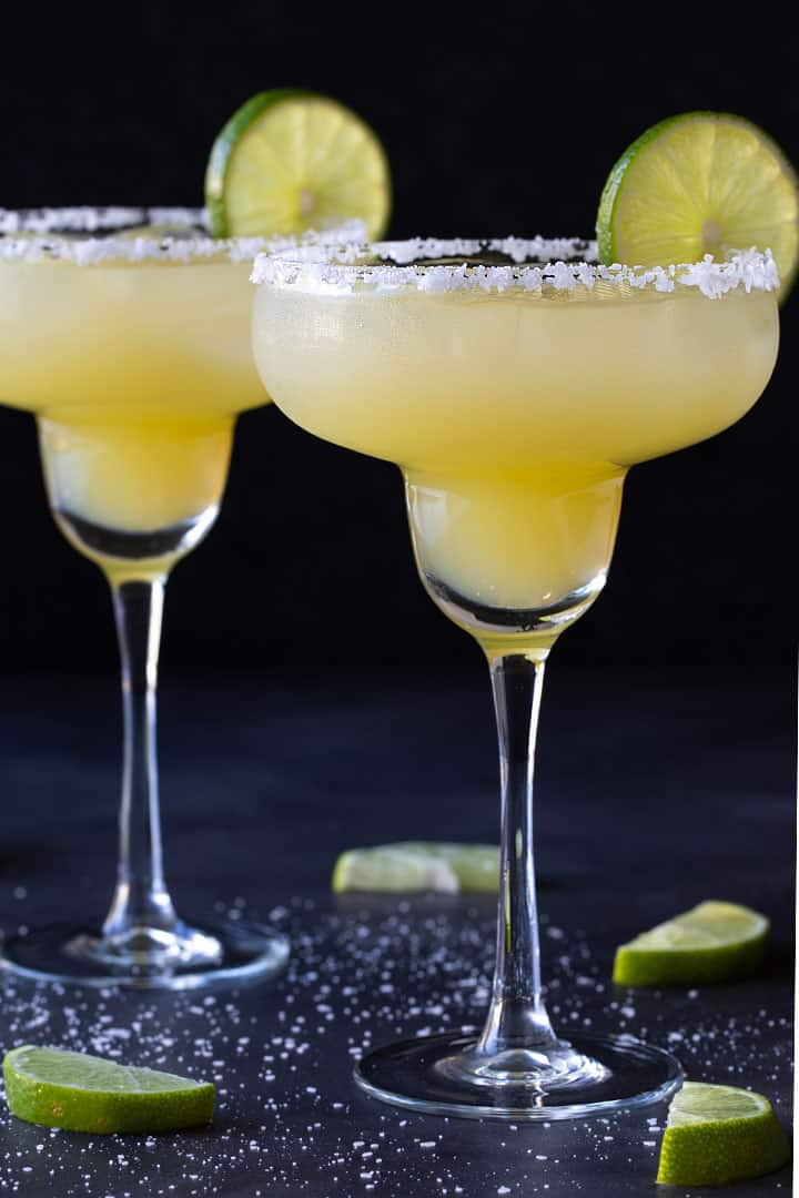 Two margaritas in glasses rimmed with salt and garnished with lime wheels.