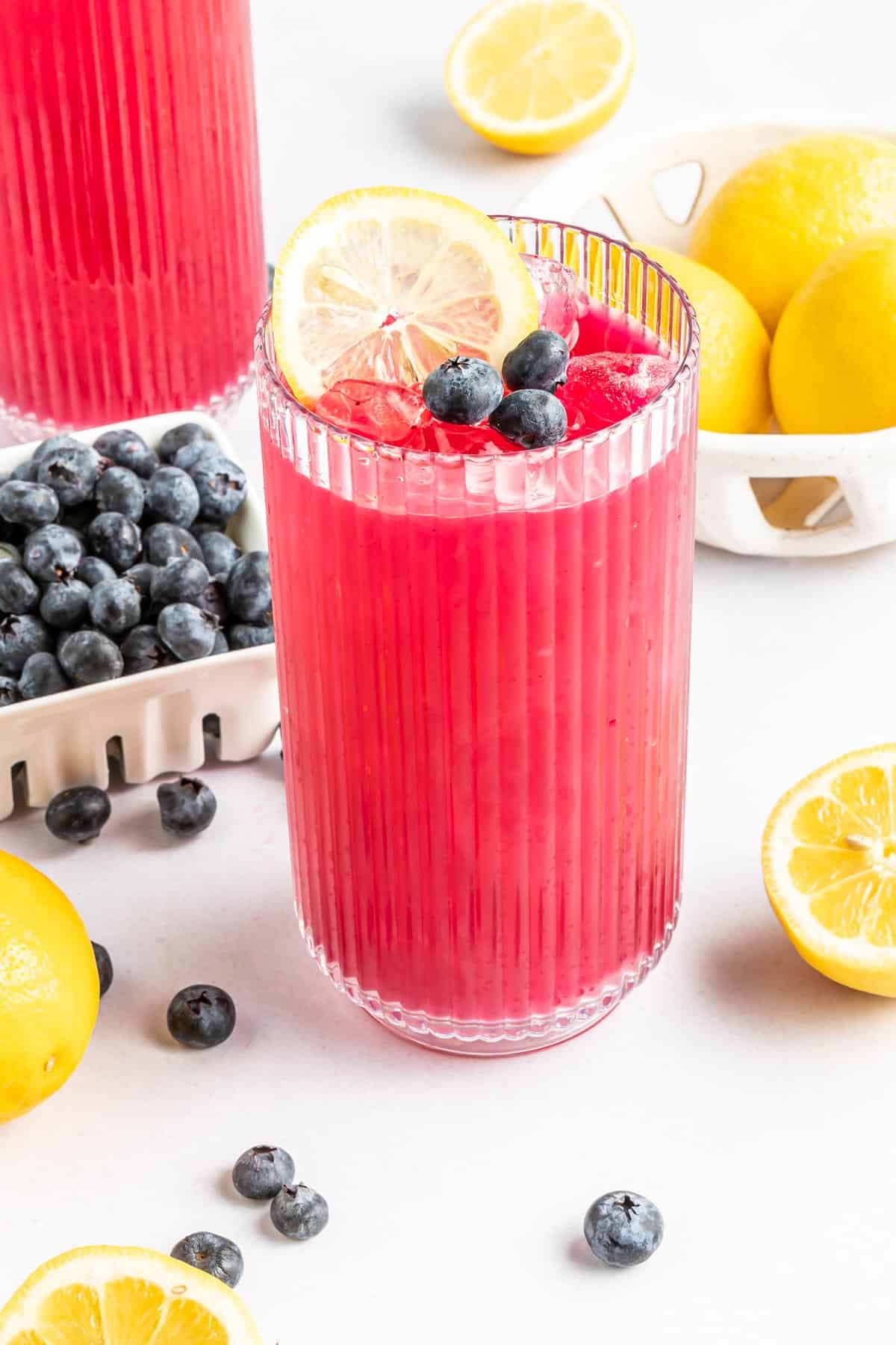 A glass of blueberry lemonade garnished with sliced lemon and fresh blueberries.