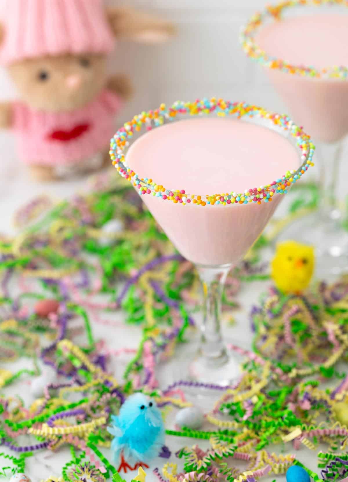 Front angled view of a pink mocktail in a glass rimmed with pastel Easter sprinkles.