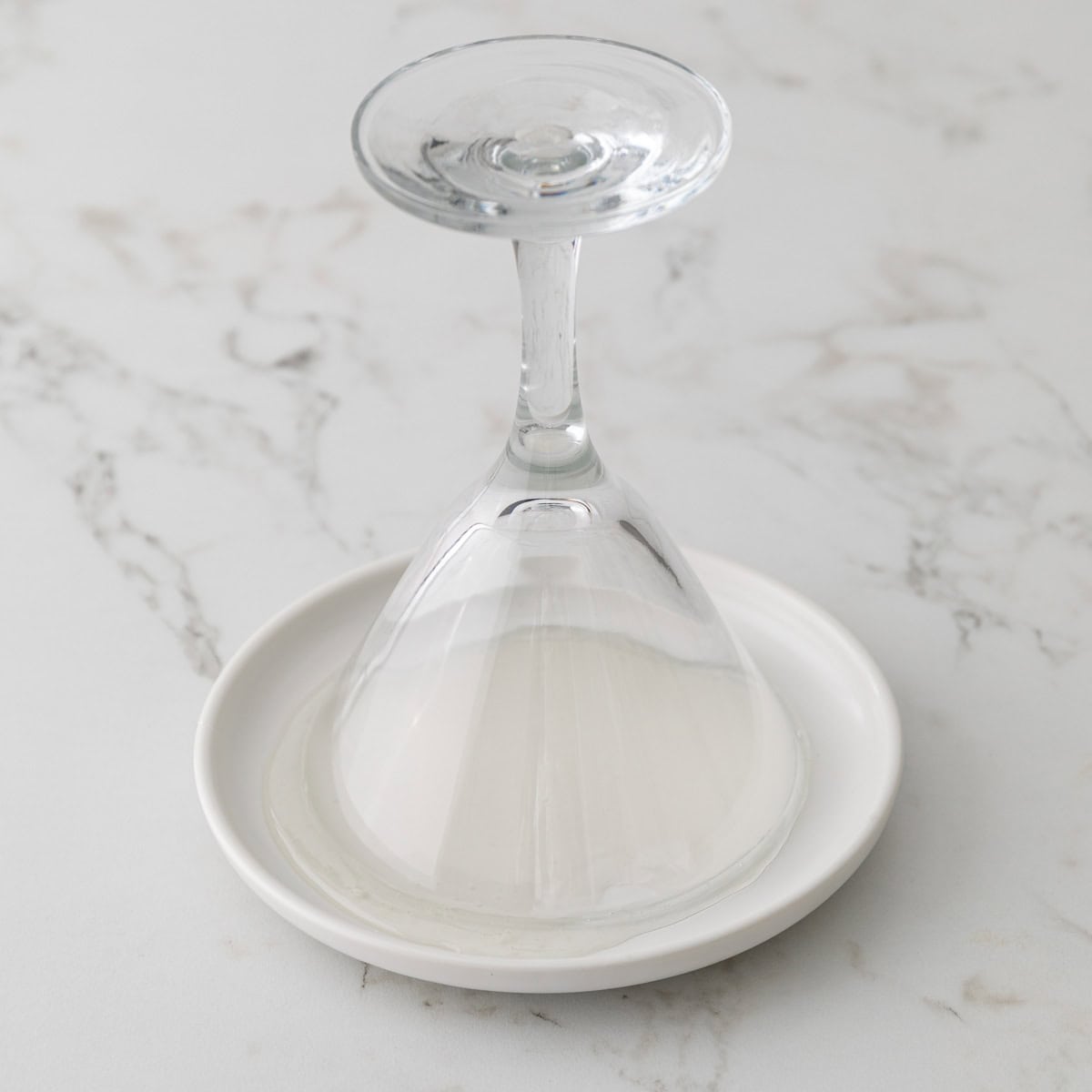 The rim of a martini glass is being dipped into a plate with corn syrup.