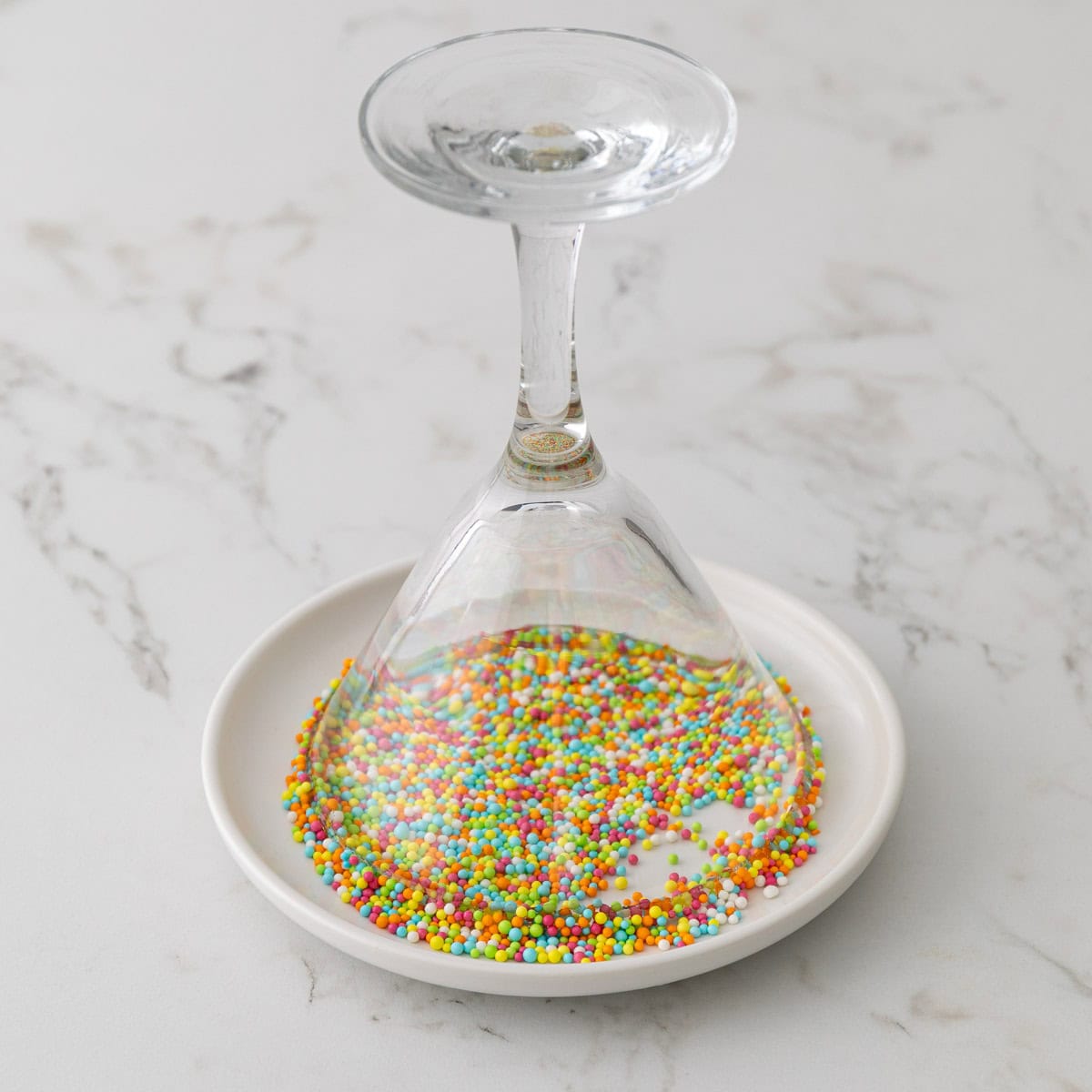 The rim of a martini glass is being dipped into a plate with Easter sprinkles.