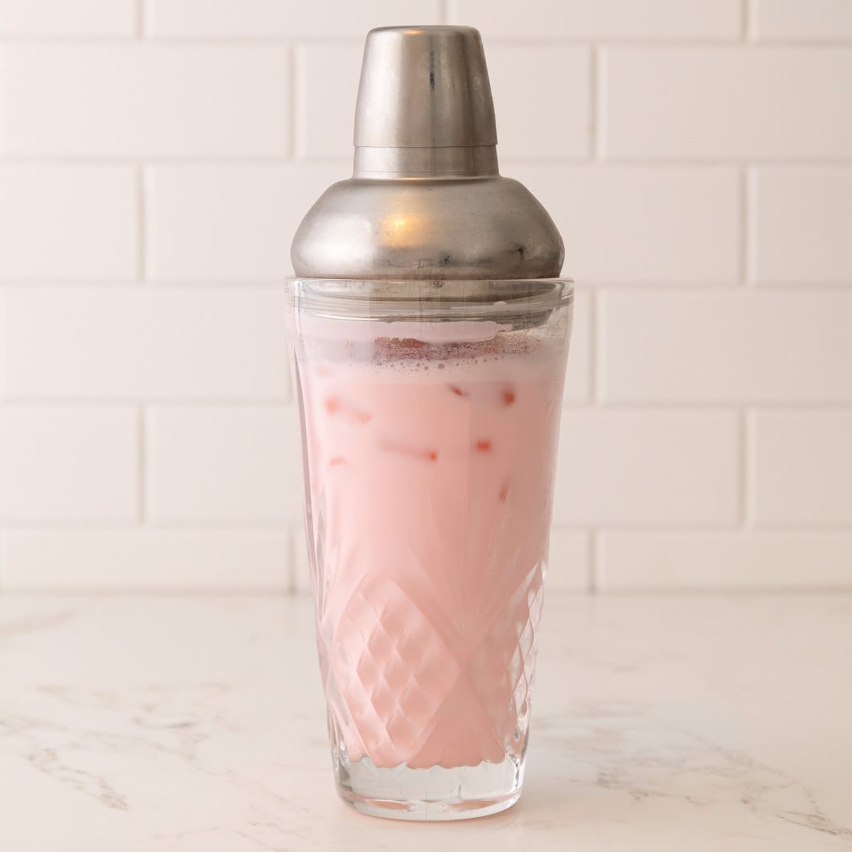 Front view of a pink mocktail in a shaker with ice.