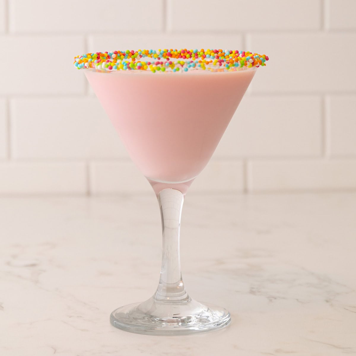 Front view of a pink mocktail in a martini glass rimmed with pastel Easter sprinkles.